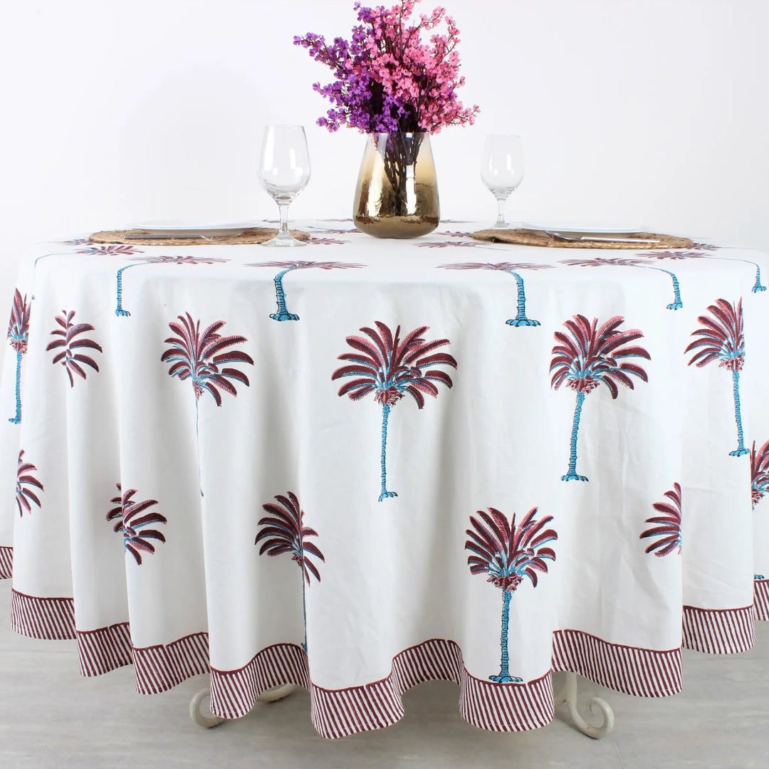 Tablecloth with palm tree design on a table set with glasses and a vase of flowers.