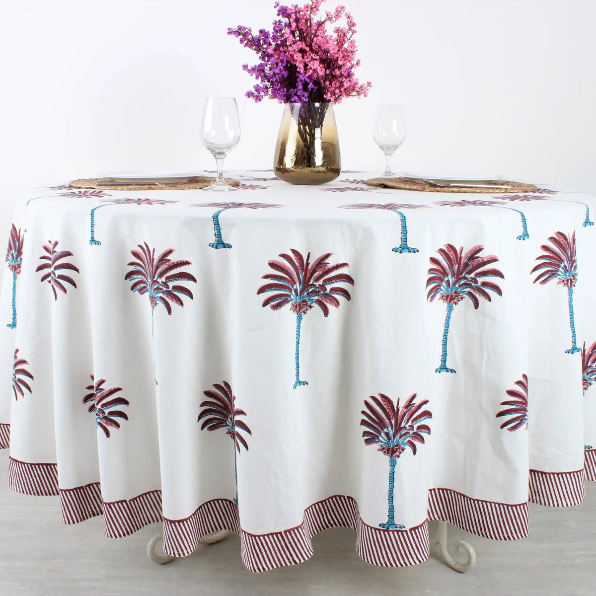 Tablecloth with palm tree design on a table set with glasses and a vase of flowers.