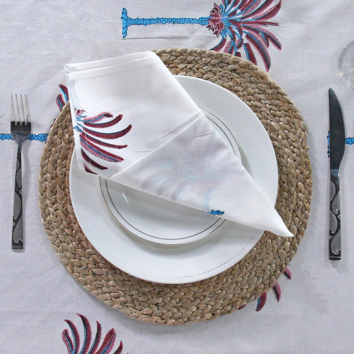 Decorative tablecloth with red and white palm tree pattern on a plain background with striped border