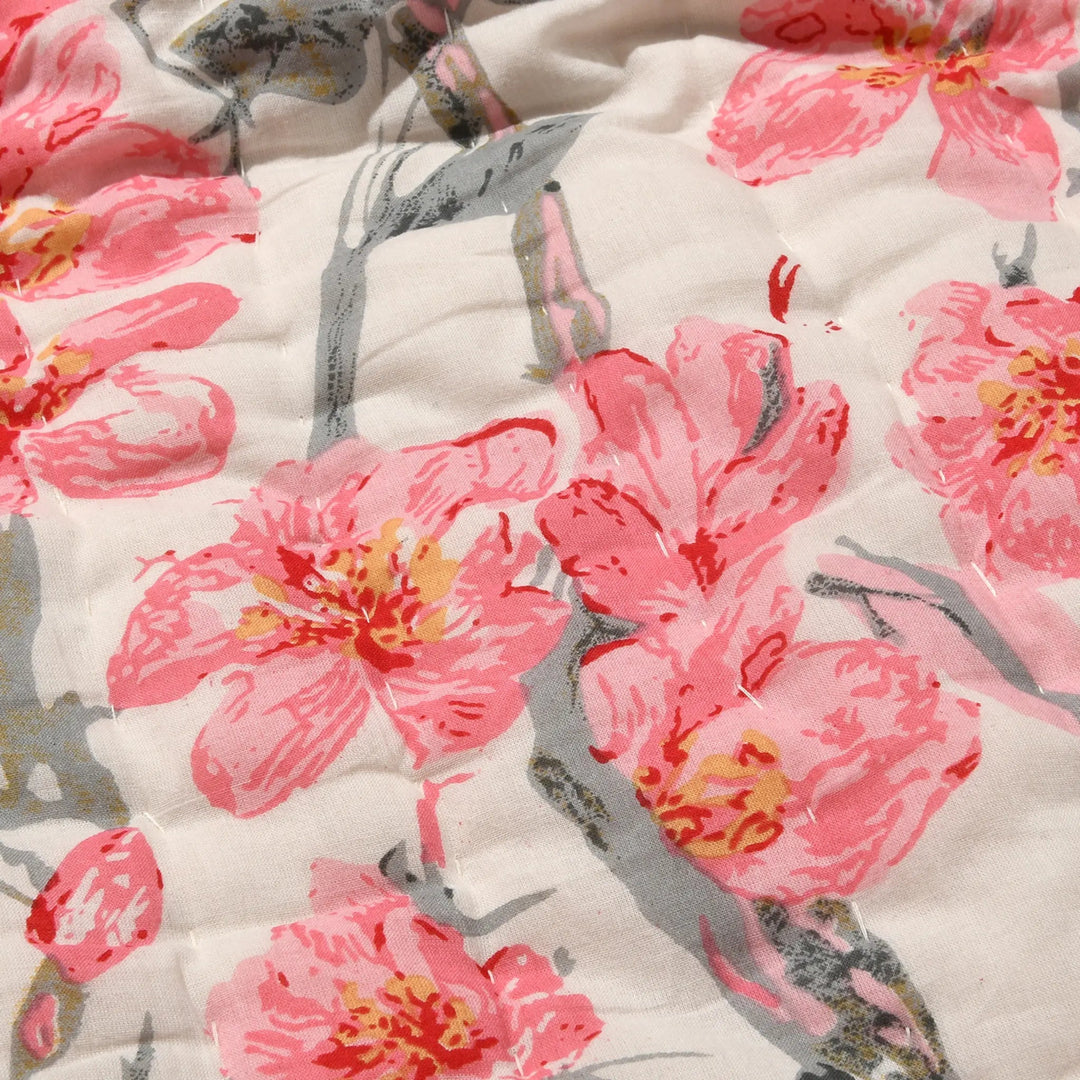 Close-up of a floral quilt with pink flowers and gray leaves on a white background
