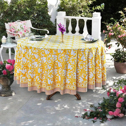 Outdoor table setting with a yellow floral tablecloth, chairs, and decorative elements.