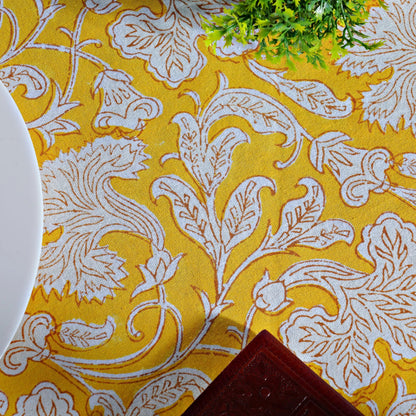 Yellow fabric with white floral pattern, partially covering a plant and a plate.