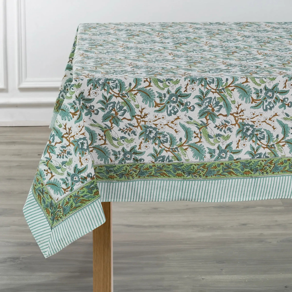 Green floral patterned tablecloth on a wooden table with a white wall background