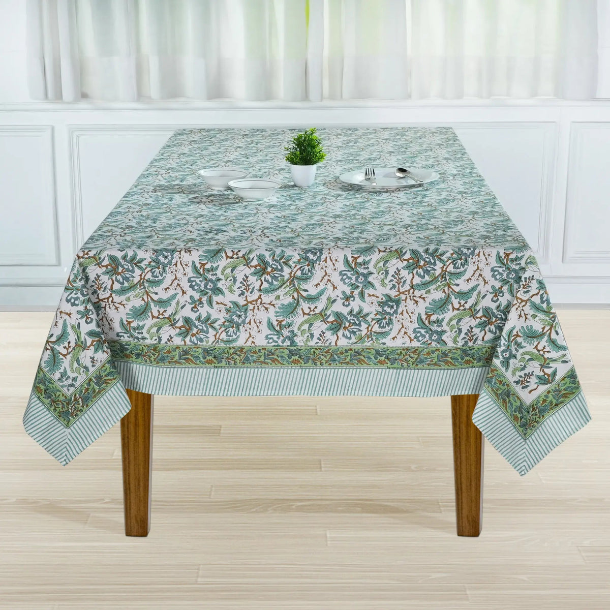 Tablecloth with floral pattern on a wooden table in a room with white curtains.