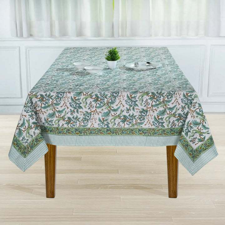 Tablecloth with floral pattern on a wooden table in a room with white curtains.