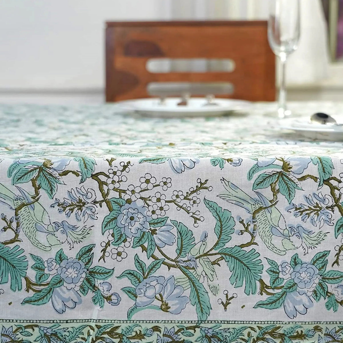 Floral and bird patterned tablecloth on a dining table with a blurred background