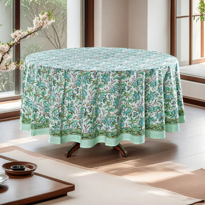 Round table with a floral tablecloth in a bright room with large windows.