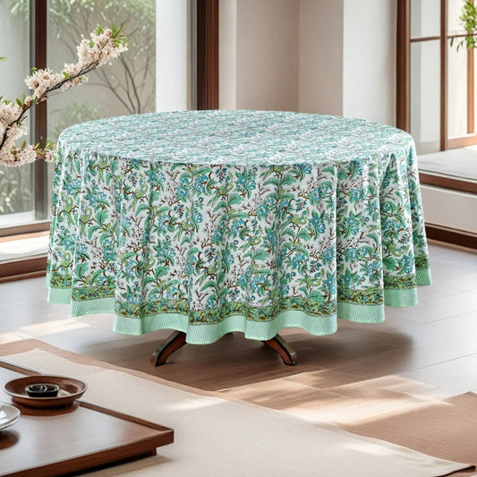 Round table with a floral tablecloth in a bright room with large windows.
