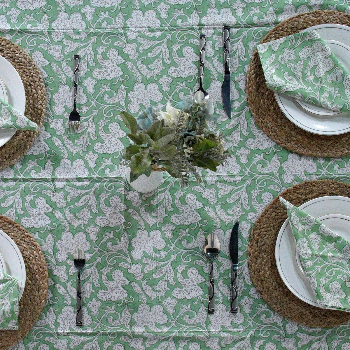 Table setting with green and white patterned tablecloth, plates, napkins, and cutlery.