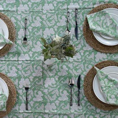 Table setting with green and white patterned tablecloth, plates, napkins, and cutlery.