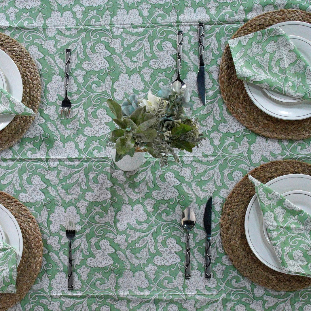 Table setting with green and white patterned tablecloth, plates, napkins, and cutlery.