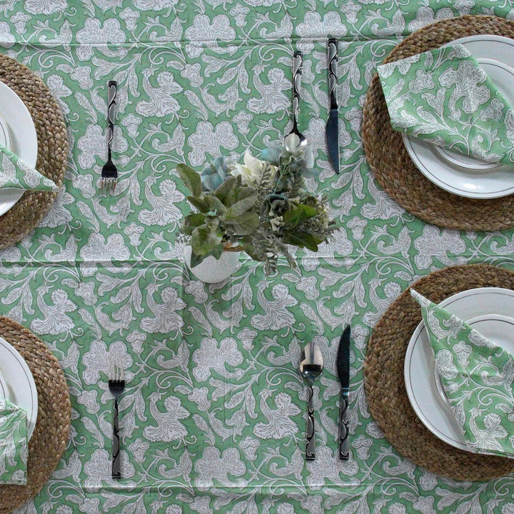 Table setting with green and white patterned tablecloth, plates, napkins, and cutlery.