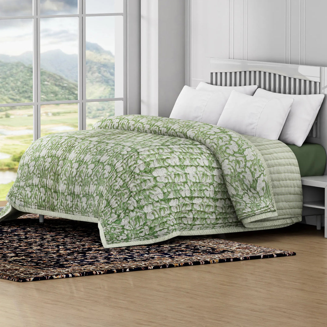 Green floral quilt on a bed in a room with large windows showing a scenic view.