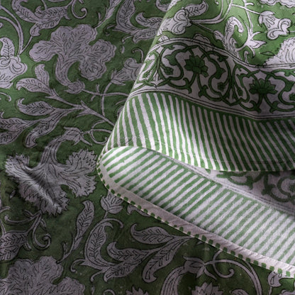 Green fabric with intricate patterns and a folded green and white striped fabric on top