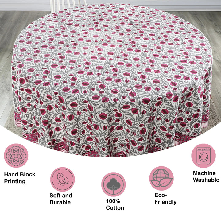 Round tablecloth with pink floral pattern on a wooden floor, featuring icons and text about material and care.