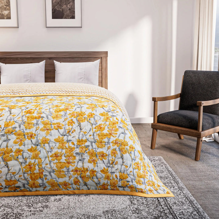 Bedroom with a bed covered in a yellow floral comforter, gray armchair, and framed artwork on the wall.