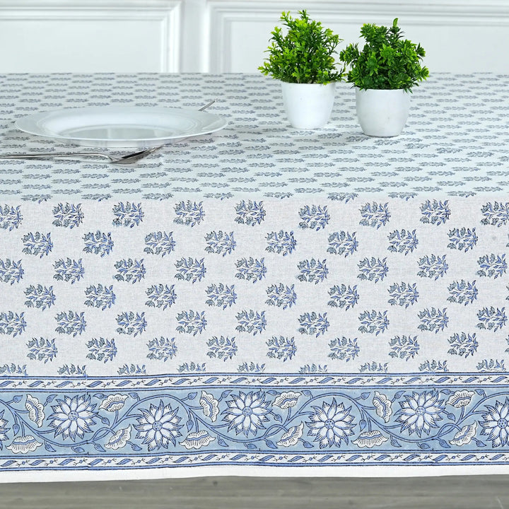 Tablecloth with blue floral pattern on a table with plants and plates.
