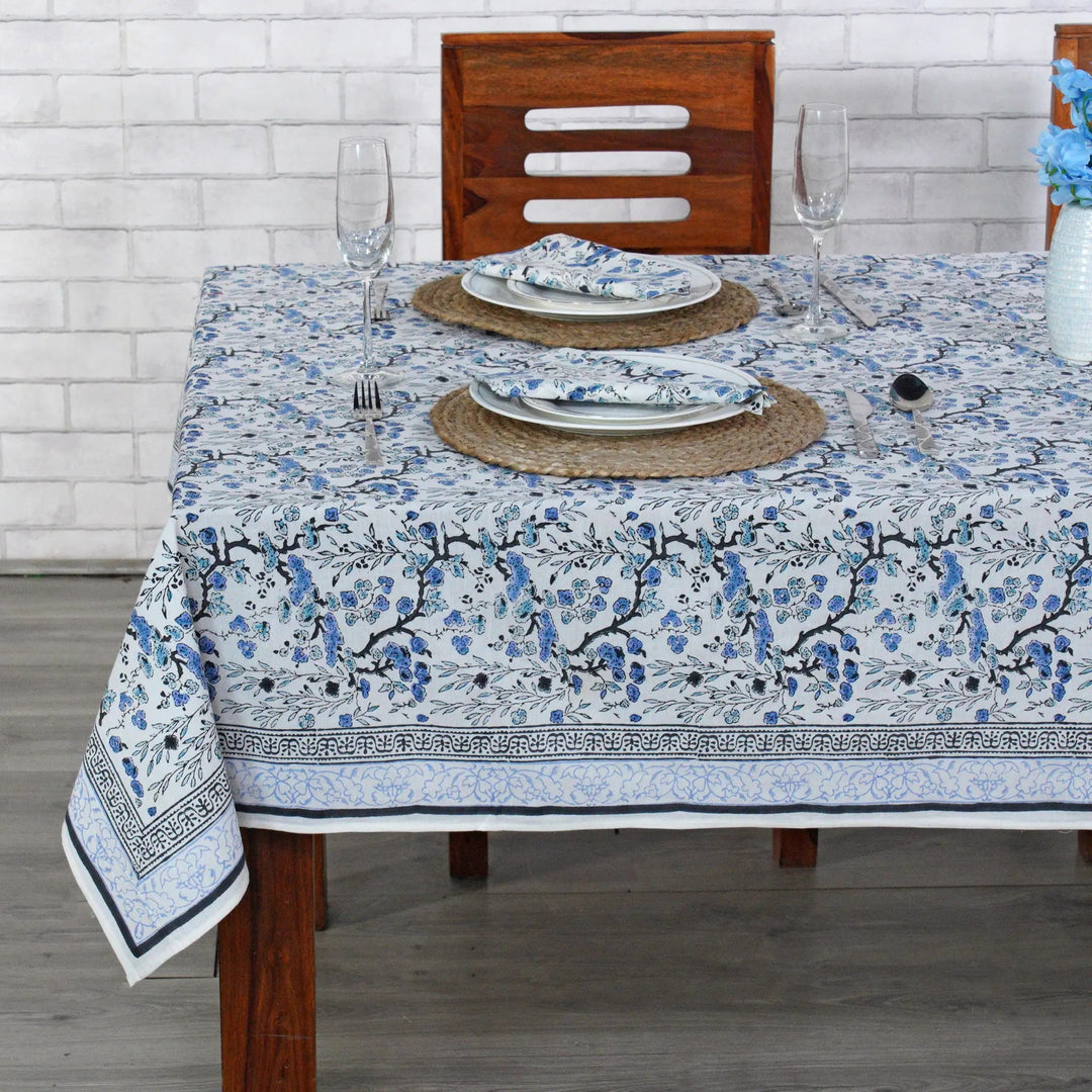 Dining table set with a floral tablecloth, plates, and glasses on a wooden table.