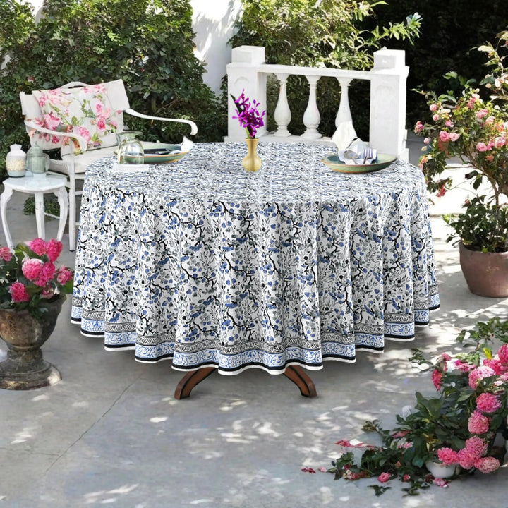 Outdoor table setting with a floral-patterned tablecloth, chairs, and decorative elements.