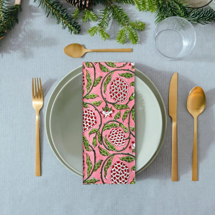 Table setting with a floral-patterned napkin, gold cutlery, and greenery on a gray tablecloth.