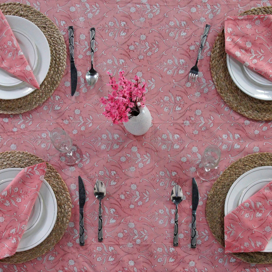 Dining table setting with pink floral tablecloth, plates, cutlery, and napkins.