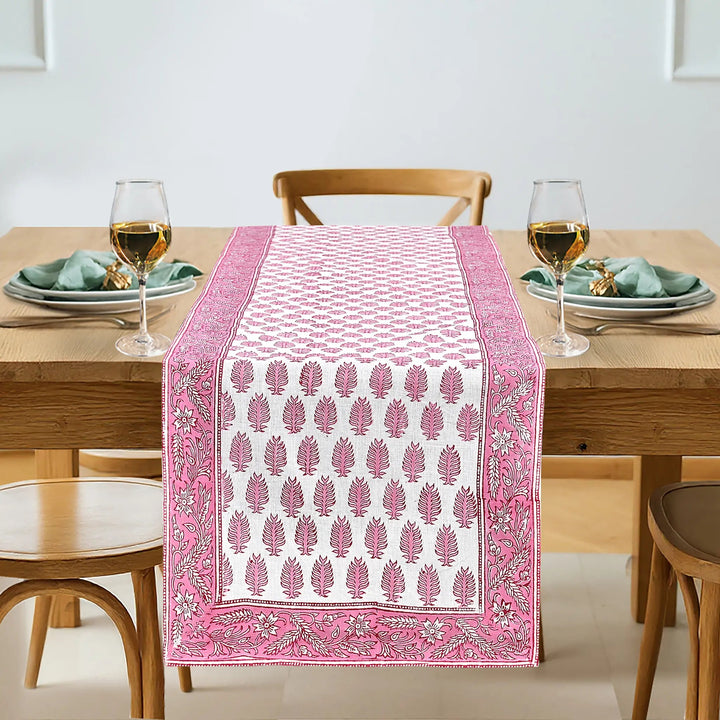 Dining table with a pink and white patterned table runner, glasses, and plates.