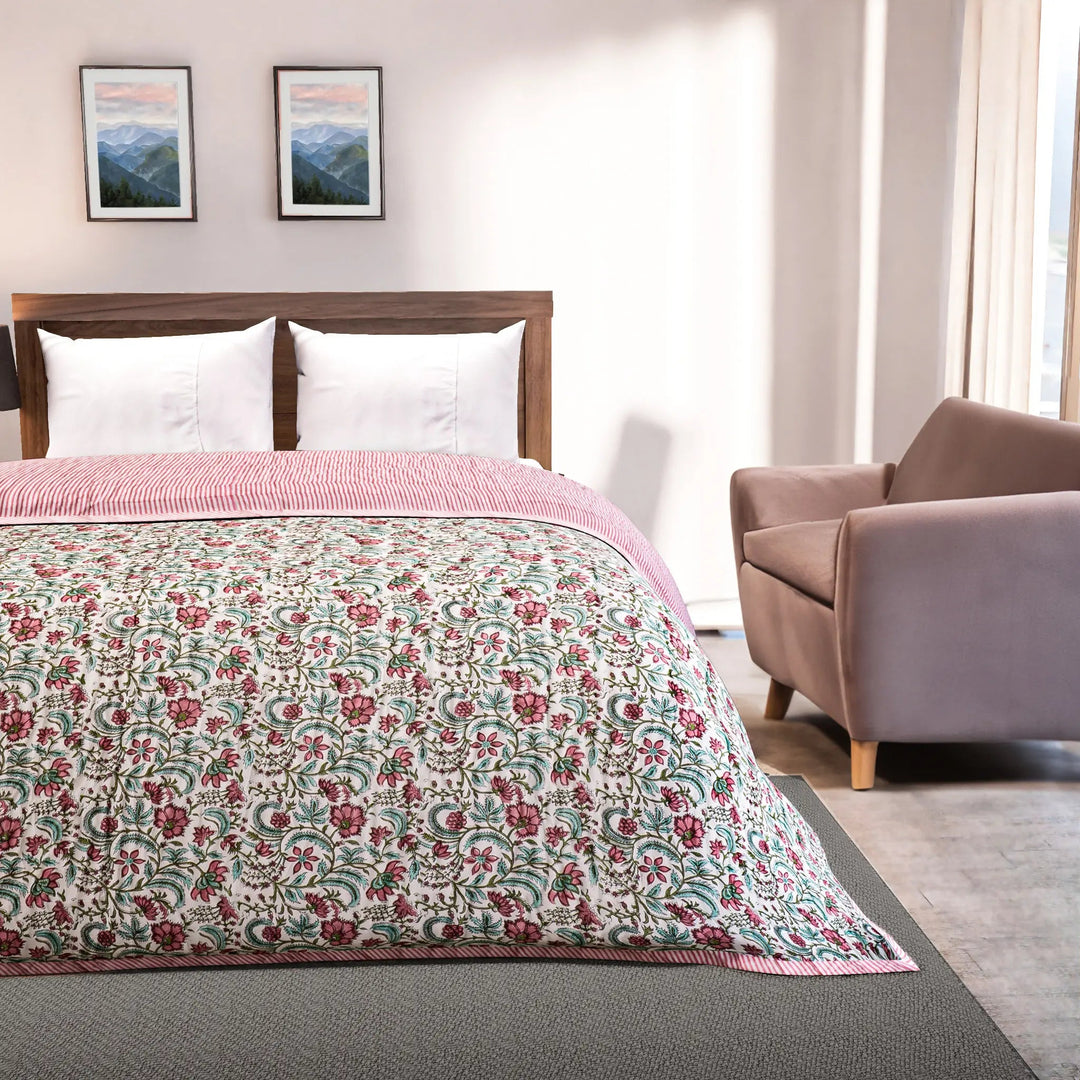 Bedroom with floral quilt on a bed, armchair, and framed pictures on the wall.