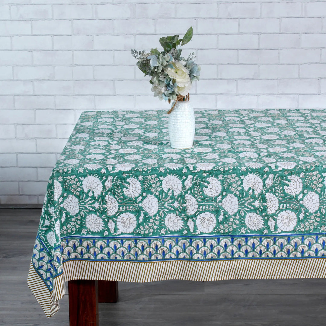 Tablecloth with floral pattern on a wooden table against a white brick wall.