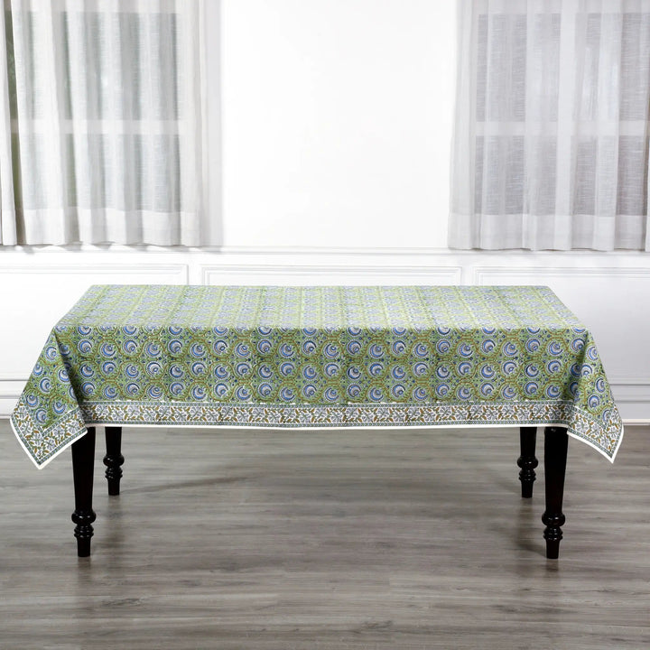 Tablecloth with green and white pattern on a wooden table in a room with white curtains.