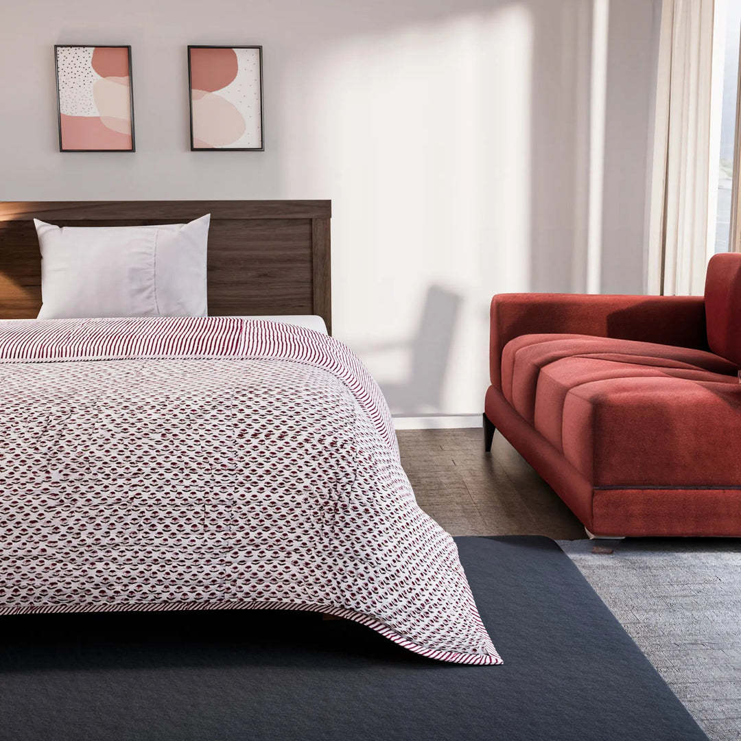 Bedroom with a bed covered in a patterned comforter and a red sofa.